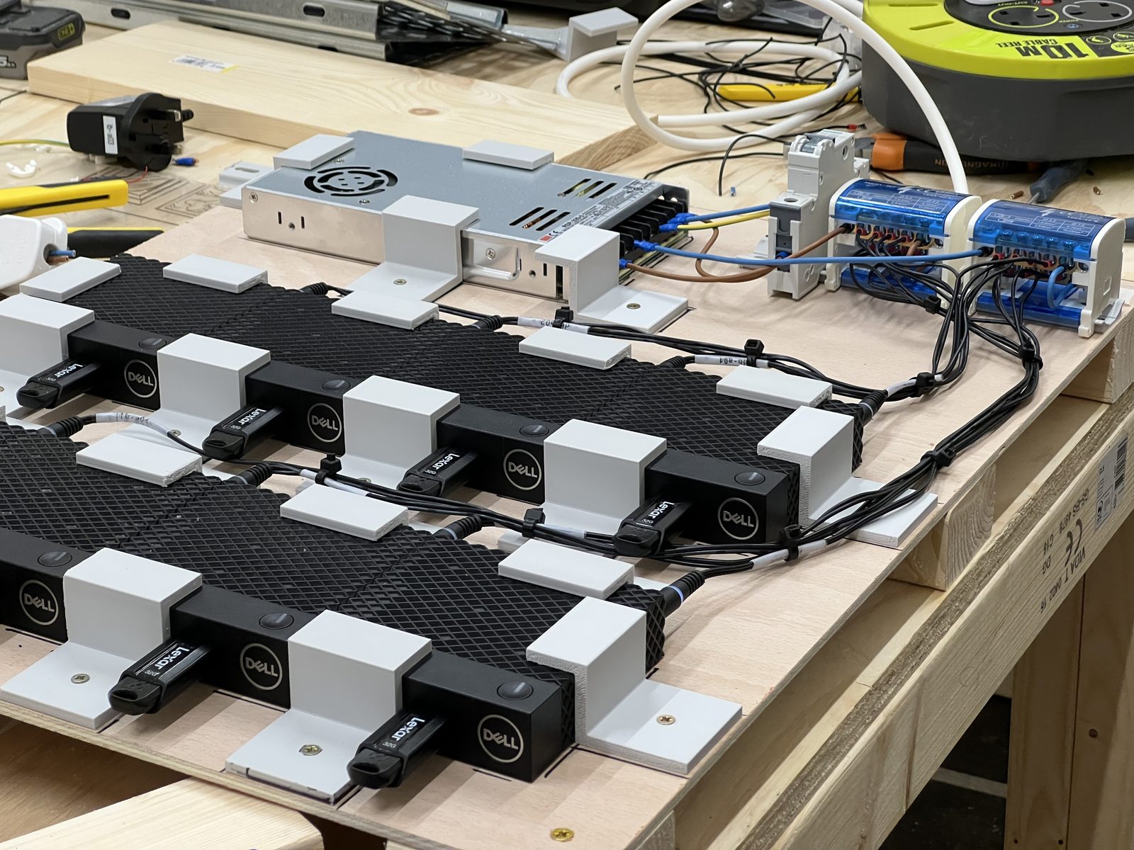 Rows of Dell thin clients mounted on 3D-printed brackets, wired to a shared power supply and breaker - a cluster mid-build.