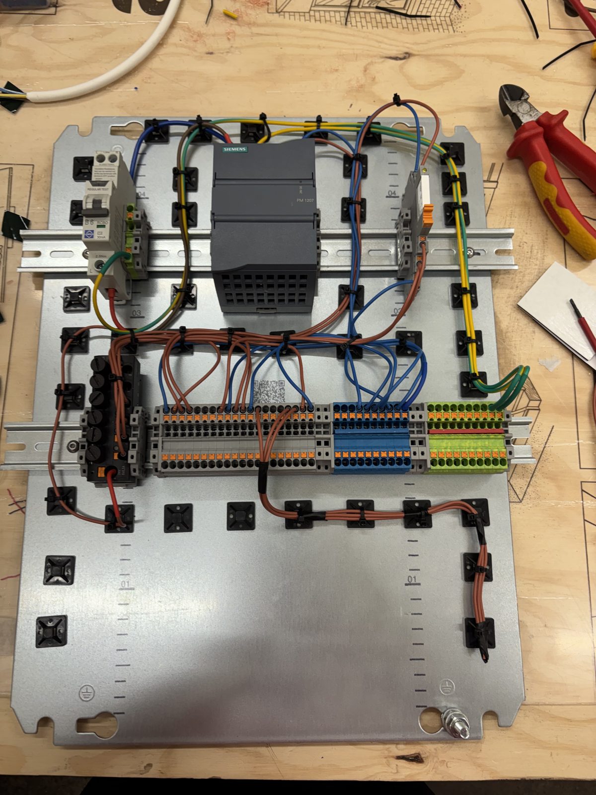 An electrical back panel mid-build: a Siemens PLC power supply, DIN rail terminal blocks and neatly tied wiring runs.