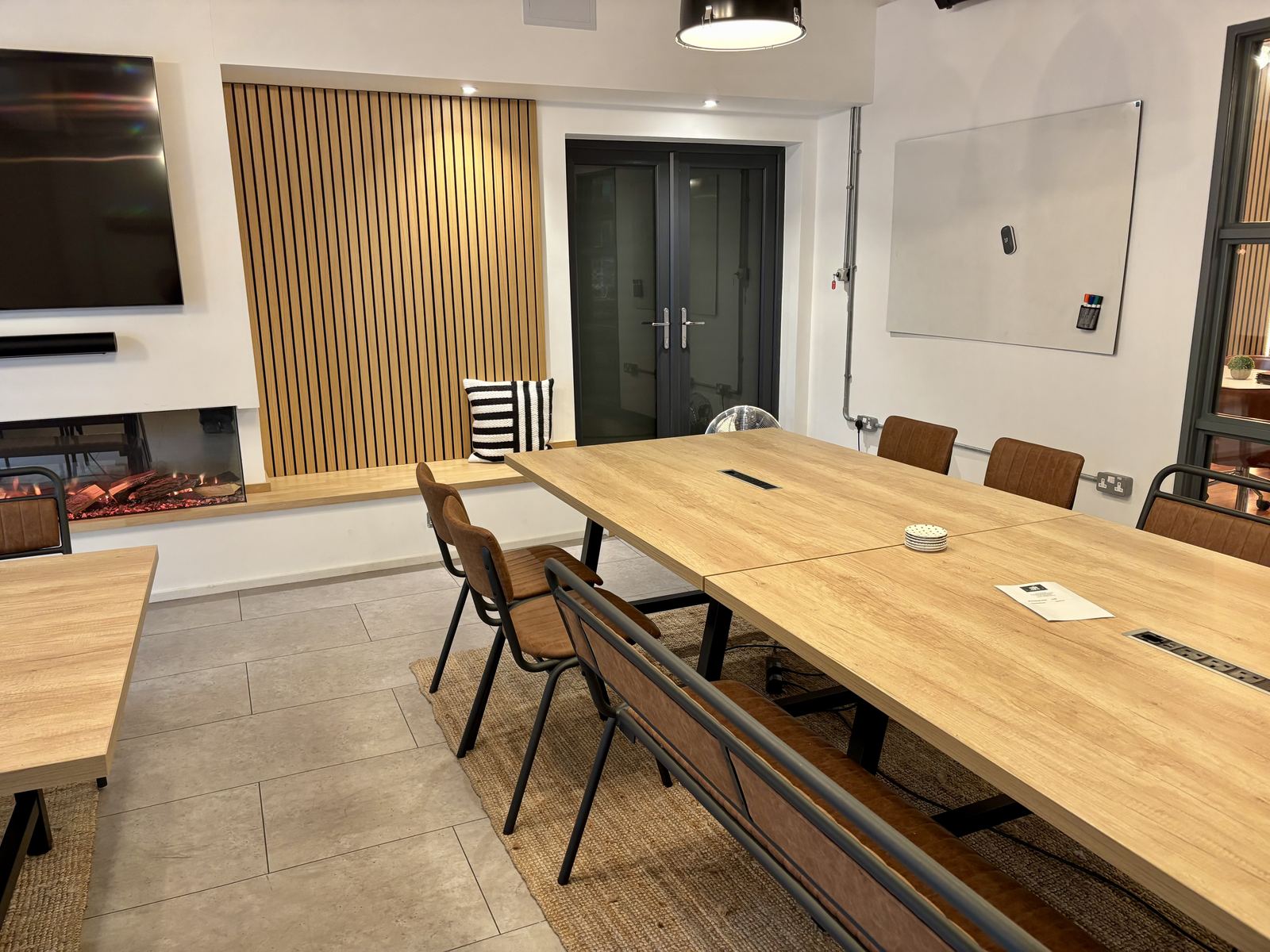 The other end of the room: a large screen and a whiteboard on the wall, a slatted oak panel and a fire, with tables in front.